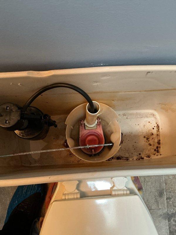 Responded to service call for water leak at toilet base near mounting bolts. Upon inspection, found active water seepage around closet bolts at the toilet-to-floor connection. Placed absorbent towels and containment materials around the base to prevent water damage to flooring. Removed tank lid to inspect internal components and identify potential contributing factors. Observed mineral deposits and corrosion within tank indicating age-related deterioration. Documented conditions with photographs showing leak location, surrounding area, and internal tank components. Leak appears to originate from compromised wax ring seal or deteriorated closet bolt gaskets requiring toilet removal and reinstallation with new sealing components.