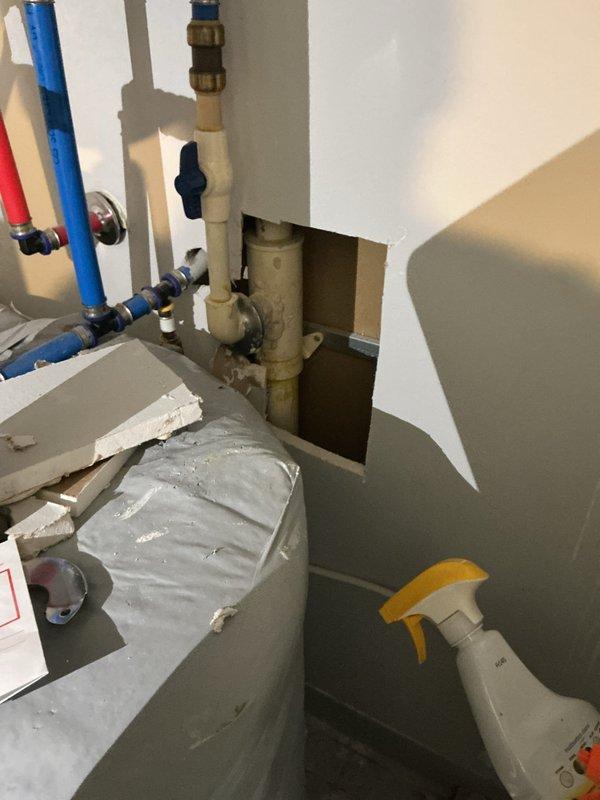 Responded to main line leak in unit 207 where customer had already opened wall access. Accessed plumbing assembly through existing cutout revealing corroded piping with active leak at valve connections. Replaced deteriorated main line section including installation of new brass fittings, shutoff valves with black, blue, and red handles for system isolation, and flanged connections. Addressed significant rust and corrosion on existing elbow sections. Integrated new PEX supply lines (blue tubing) with existing copper and galvanized steel piping. Installed pressure regulation components and ensured proper valve operation for future maintenance access. Protected toilet fixture during work and verified system integrity with pressure testing before closing.