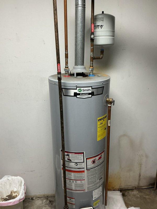 Responded to service call for water heater leaking from bottom in utility closet. Upon arrival, inspected A.O. Smith tanked water heater and confirmed active leak originating from base of unit. Evaluated tank condition and determined internal tank failure causing water discharge onto concrete floor. Documented existing installation including copper supply lines, expansion tank, and flue venting system. Due to compromised tank integrity and safety concerns, recommended immediate replacement of failed water heater unit. Coordinated with property manager for approval and scheduling of replacement installation.