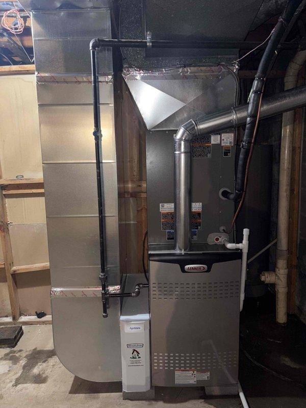 Completed full HVAC system installation including an 80% efficiency Lennox furnace in the basement mechanical room and matching Lennox air conditioning condenser unit on exterior pad. The furnace installation features proper flexible ductwork connections to the existing ventilation system, metal plenum integration for air distribution, and appropriate gas piping and electrical conduit runs. The outdoor condensing unit was positioned on a level platform pad against the home's exterior with proper clearances from the structure, connected via refrigerant lines and electrical service to complete the split system configuration.