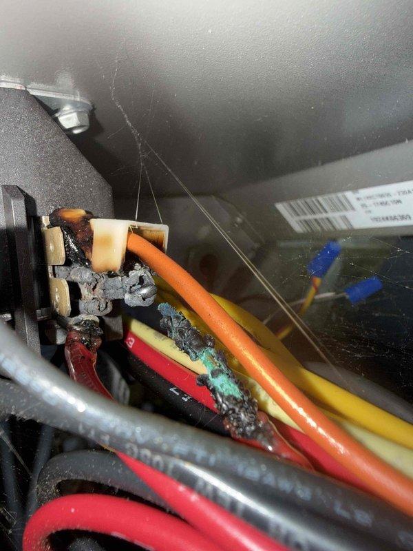 Responded to no cooling complaint on one-year-old air conditioning system with indoor temperature at 80 degrees. Upon inspection, discovered severe thermal damage and melted insulation at wire connections in the electrical junction area, with visible charring, corrosion, and debris buildup indicating an electrical fault or overheating event. Documented damaged connections with photographs showing compromised wire insulation and corroded terminal blocks requiring immediate repair to restore proper system operation and prevent potential safety hazards.
