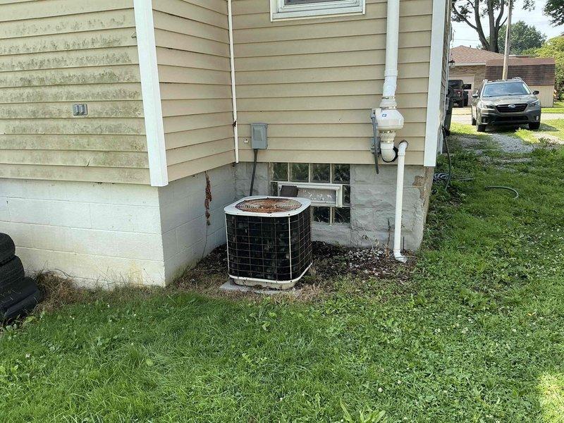 Conducted on-site evaluation of 30-year-old residential air conditioning system showing significant age-related deterioration. Exterior condensing unit exhibited substantial rust and corrosion on top surface, housed in protective cage adjacent to home's foundation with electrical service panel and PVC condensate drainage nearby. Interior inspection revealed beige furnace/air handler unit in basement mechanical room with standard ductwork configuration and water heater installation. Documented equipment condition through photographic evidence and provided comprehensive replacement estimate due to advanced age of system and extent of corrosion present on outdoor unit.