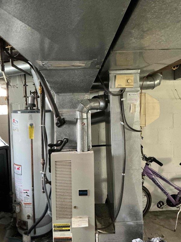 Conducted on-site evaluation of 30-year-old residential air conditioning system showing significant age-related deterioration. Exterior condensing unit exhibited substantial rust and corrosion on top surface, housed in protective cage adjacent to home's foundation with electrical service panel and PVC condensate drainage nearby. Interior inspection revealed beige furnace/air handler unit in basement mechanical room with standard ductwork configuration and water heater installation. Documented equipment condition through photographic evidence and provided comprehensive replacement estimate due to advanced age of system and extent of corrosion present on outdoor unit.