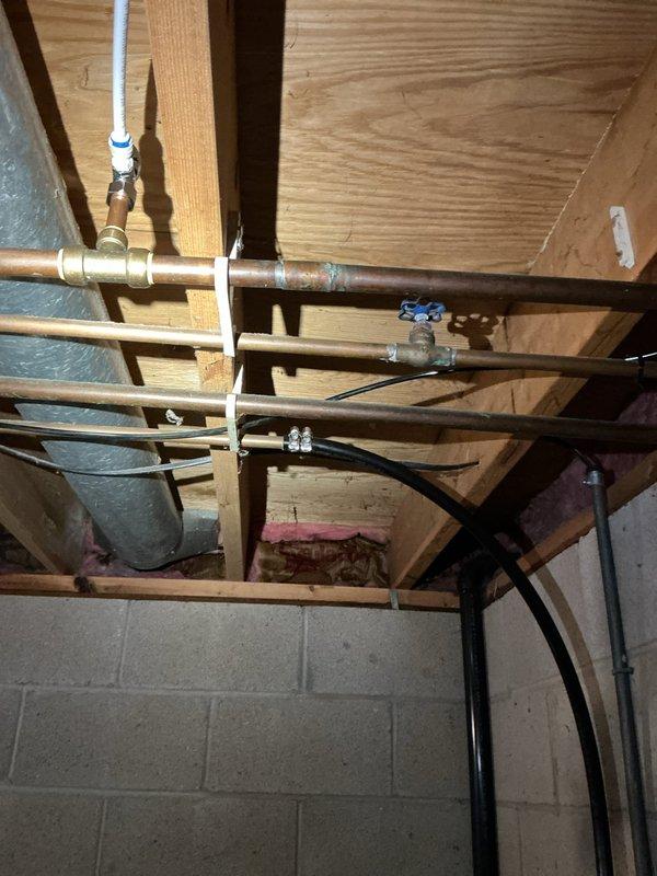 Installed new utility sink in garage where no previous plumbing existed. Ran supply and drain lines through wall from basement utility area, connecting to existing plumbing infrastructure visible in exposed ceiling joists. Completed rough-in plumbing work including copper supply lines with shutoff valves and PVC drainage system routed along foundation wall to tie into main drain stack.