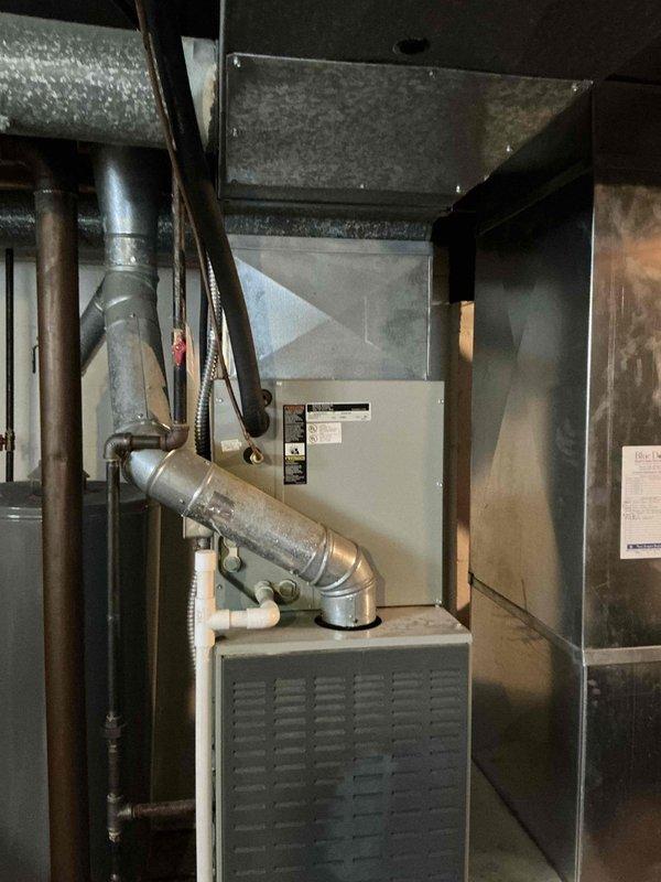 Completed estimate for replacement of 22-year-old residential HVAC system currently providing cooling. Inspected existing basement furnace installation with triangular filter access panel and associated ductwork, along with exterior condensing unit positioned on concrete pad with electrical conduit and utility connections. Documented equipment condition and provided replacement quote for aging system.