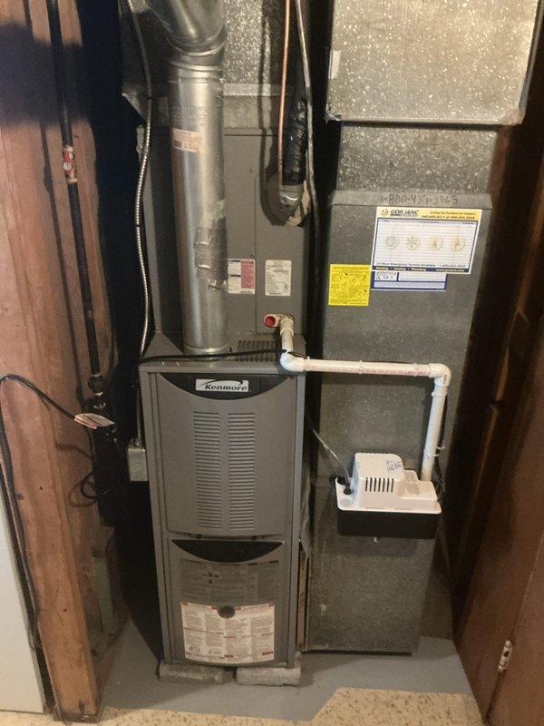 Completed full HVAC system installation including an 80% efficiency furnace and air conditioning system. The indoor Kenmore furnace unit and air handler were installed in the basement utility area with proper metallic supply ductwork connections, PVC condensate drainage lines, and gas piping. The outdoor condensing unit was positioned on a new concrete pad against the brick exterior with appropriate electrical disconnect box, conduit runs, and service clearances for maintenance access.