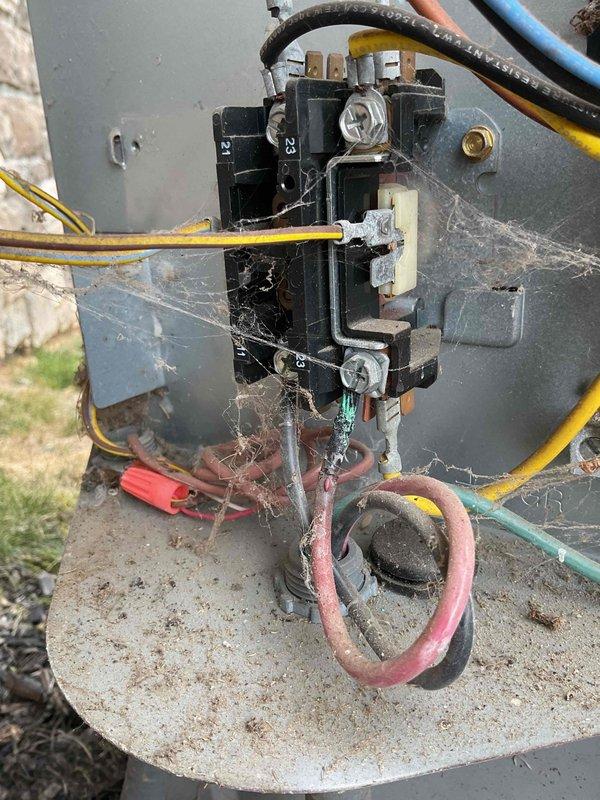 Responded to no-cooling complaint on 12-year-old outdoor air conditioning unit. Upon arrival, found contactor assembly and capacitor heavily covered in cobwebs and debris, indicating lack of recent maintenance. Inspected electrical connections and found aged, worn wiring throughout the unit. Observed 45/5µF dual-run capacitor rated at 370V AC with multiple wire connections. Cleaned contactor assembly and surrounding electrical components, removing extensive spider web accumulation from relay contacts, terminals, and wiring connections. Verified all wire connections were secure at contactor and capacitor terminals. Tested contactor operation and capacitor functionality. System restored to proper cooling operation following cleaning and inspection of electrical components.
