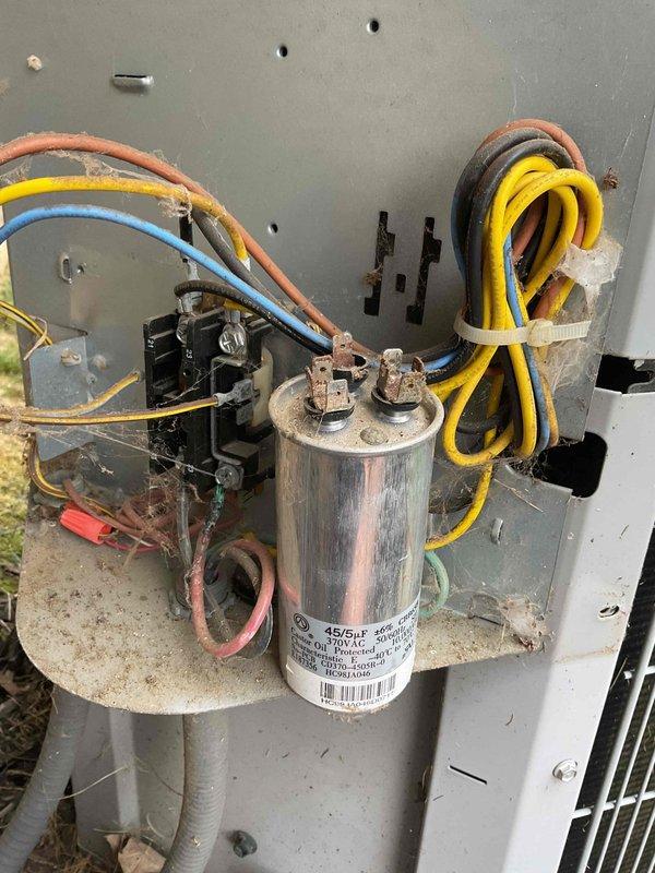 Responded to no-cooling complaint on 12-year-old outdoor air conditioning unit. Upon arrival, found contactor assembly and capacitor heavily covered in cobwebs and debris, indicating lack of recent maintenance. Inspected electrical connections and found aged, worn wiring throughout the unit. Observed 45/5µF dual-run capacitor rated at 370V AC with multiple wire connections. Cleaned contactor assembly and surrounding electrical components, removing extensive spider web accumulation from relay contacts, terminals, and wiring connections. Verified all wire connections were secure at contactor and capacitor terminals. Tested contactor operation and capacitor functionality. System restored to proper cooling operation following cleaning and inspection of electrical components.