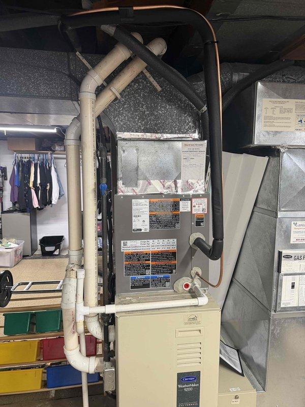 Completed installation of Carrier air conditioning system with evaporator coil and air handler unit in basement utility area. Installed new condensate drain lines using white PVC piping with proper trap configuration, mounted condensate pump with electrical connection on equipment platform, and connected refrigerant lines with appropriate insulation. All equipment properly positioned on elevated platform, ductwork connected to air handler with flexible transitions, and system tested for proper operation.