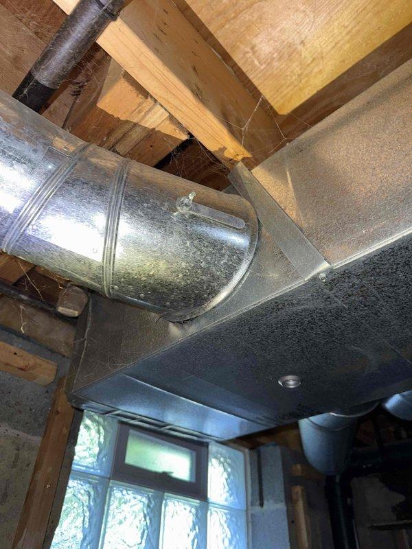 Responded to complaint of inadequate cooling in upstairs zone with 7-degree temperature differential between floors. Inspected HVAC system infrastructure including main supply ductwork, distribution branches, and basement mechanical components. Documented existing ductwork configuration showing large metallic supply trunk and flexible duct connections running through basement ceiling joists. Evaluated airflow distribution system serving multi-level residence with 3-year-old air conditioning unit. Photos captured of ductwork layout, insulation conditions, and overall system installation for assessment of potential airflow restrictions or zoning issues affecting upper level temperature control.