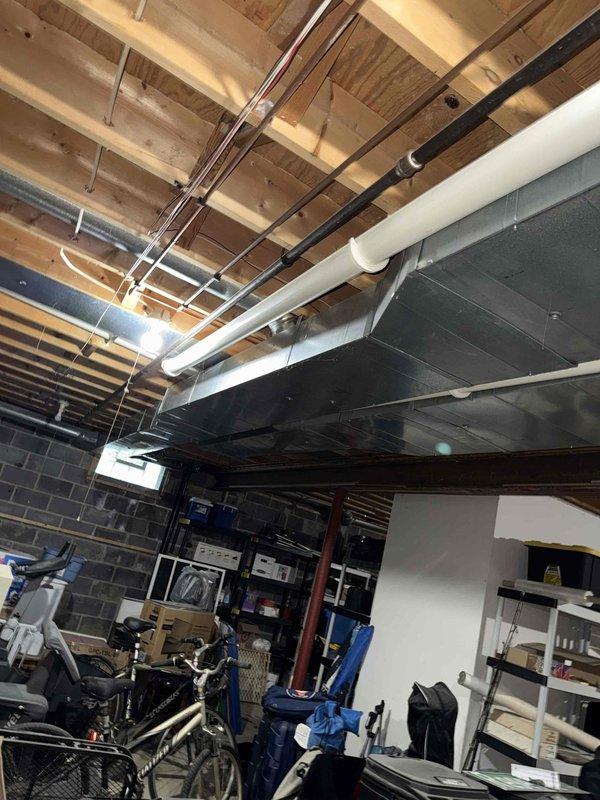 Responded to complaint of inadequate cooling in upstairs zone with 7-degree temperature differential between floors. Inspected HVAC system infrastructure including main supply ductwork, distribution branches, and basement mechanical components. Documented existing ductwork configuration showing large metallic supply trunk and flexible duct connections running through basement ceiling joists. Evaluated airflow distribution system serving multi-level residence with 3-year-old air conditioning unit. Photos captured of ductwork layout, insulation conditions, and overall system installation for assessment of potential airflow restrictions or zoning issues affecting upper level temperature control.