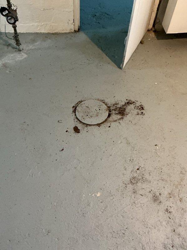 Snaked main drain line through first floor access point to the flange after toilet removal by property owner. Cleared blockage and restored proper drainage flow. Documented pre-existing conditions showing debris accumulation around floor drain and basement utility area.