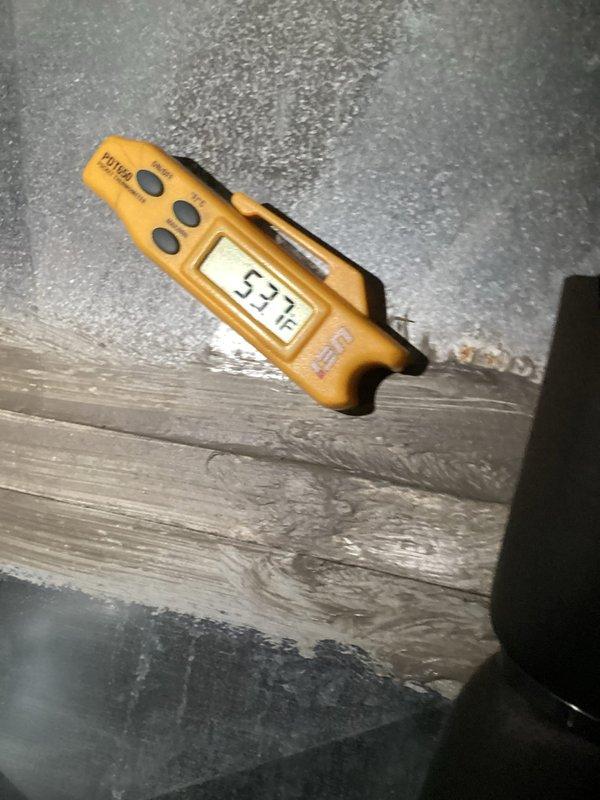 Performed routine maintenance inspection on 8-year-old air conditioning system for MVP customer. Evaluated system components including heat exchanger and recorded ambient temperature reading of 53°F in attic space. Documented equipment condition through photographic records showing HVAC unit with secured banding and temperature measurements on weathered decking, confirming system operational status.