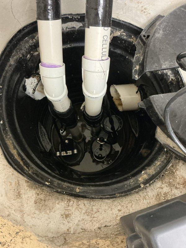 Responded to service call for water in basement with unknown source. Performed comprehensive inspection of 9-year-old sump pump system and basin to determine if equipment was contributing to water intrusion issue. Examined sump pump operation, float switches, discharge piping, and basin integrity. Verified pump functionality and checked all mechanical components submerged in basin water. Inspected PVC discharge lines, mounting assemblies, and electrical connections routed through wall-mounted conduit. Assessed concrete floor conditions around pump location, noting water exposure patterns and mineral deposits. Evaluated overall sump pump installation and drainage system to rule out equipment failure as source of basement water problem.