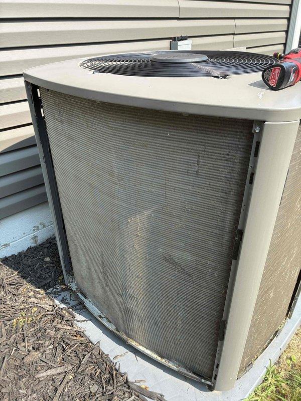 Completed MVP cooling maintenance visit on residential air conditioning system. Performed temperature diagnostics using digital thermometer, recording supply air temperature of 63.2°F to verify proper cooling operation. Inspected outdoor condenser unit, noting accumulated dirt and debris on front intake grille and coil surfaces. Unit operational at time of service with fan motor running properly. Documented equipment condition through photographs for service records.