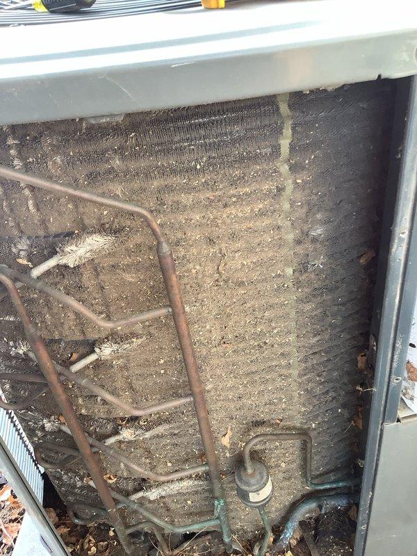 Responded to service call for non-operational outdoor AC condenser unit on 10-year-old system. Upon arrival, found outdoor unit heavily soiled with significant debris accumulation on condenser coils and internal components. Performed thorough inspection revealing excessive dirt, dust, and organic matter blocking airflow through aluminum fins and coating refrigerant coil assembly. Removed access panel and documented severe contamination on back panel and copper refrigerant lines. Cleaned condenser coils using appropriate methods to restore proper airflow and heat transfer efficiency. Cleared debris from unit base and surrounding area. Verified refrigerant line connections and electrical components for proper operation following cleaning. System restored to operational status with improved airflow and cooling capacity.