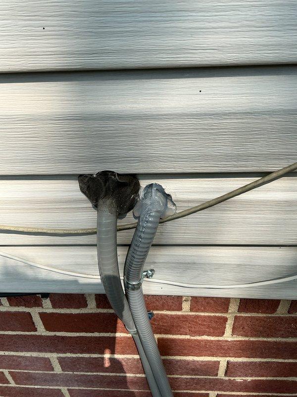 Returned to property to seal conduit penetration through exterior siding where two flexible conduits exit the building envelope. Applied black foam insulation sealant around the conduits at the penetration point to prevent pest intrusion and weather infiltration. Work was completed on the exterior of the building where vinyl siding meets the brick foundation, with customer authorization to proceed if not home.