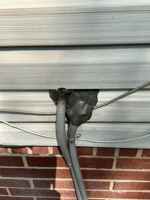 Returned to property to seal conduit penetration through exterior siding where two flexible conduits exit the building envelope. Applied black foam insulation sealant around the conduits at the penetration point to prevent pest intrusion and weather infiltration. Work was completed on the exterior of the building where vinyl siding meets the brick foundation, with customer authorization to proceed if not home.
