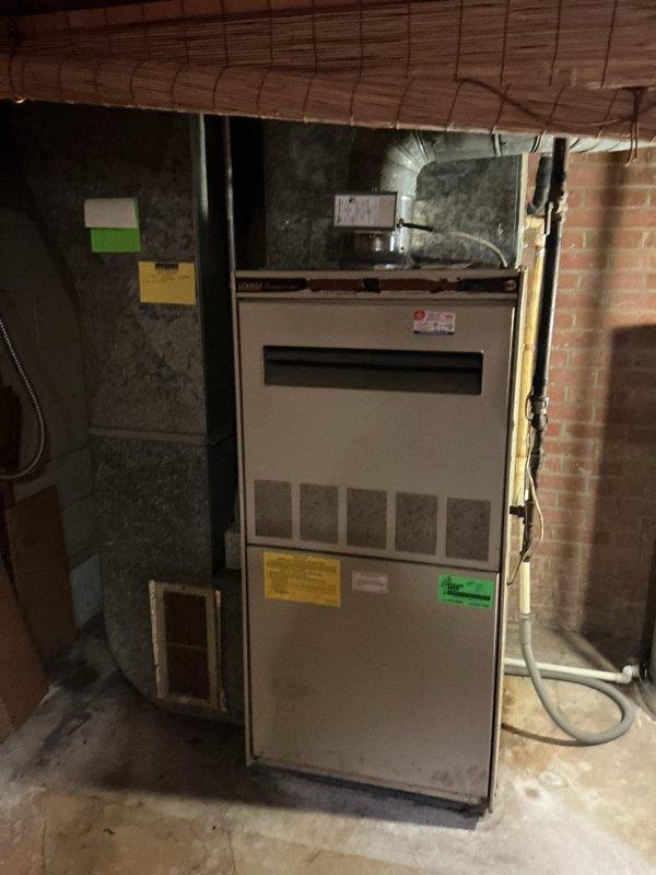 Completed full HVAC system installation including removal of existing wood burner and installation of new 80% efficiency furnace in basement mechanical room and matching air conditioning condenser unit on exterior. New furnace unit installed against concrete block wall with proper venting, ductwork connections to existing plenum, and all required electrical and gas line connections per manufacturer specifications. Exterior AC condenser positioned on grade near brick foundation with refrigerant lines run to interior air handler, electrical disconnect installed, and system charged and tested for proper operation.
