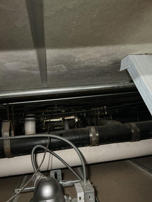 Responded to report of leaking cast-iron piping in common area ceiling cavity. Accessed ceiling space and inspected 42-year-old vertical stack system showing signs of deterioration and active water intrusion. Documented conditions of exposed piping, ductwork, and mechanical components in overhead chase, noting corrosion patterns consistent with age-related failure of cast-iron plumbing infrastructure. Photographed affected areas including stack identification markings and surrounding HVAC equipment for further assessment and repair planning.