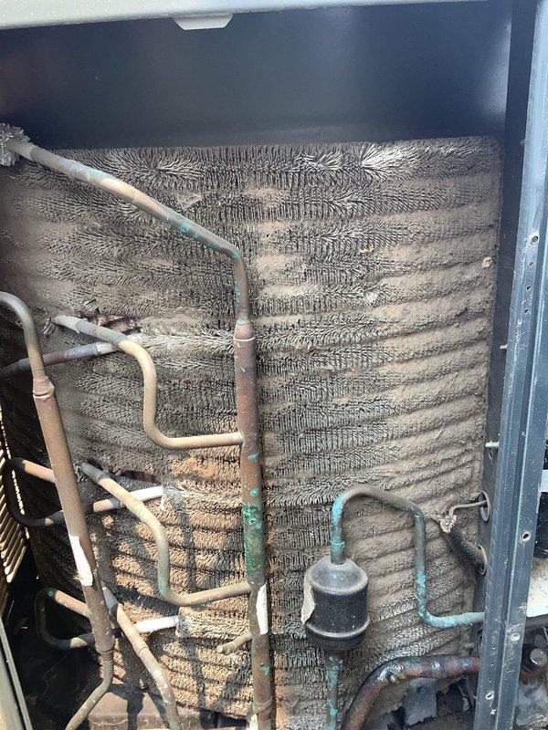 # Maintenance Service Completed on 13-Year-Old Air Conditioning System

Performed comprehensive preventive maintenance on a residential split-system air conditioner. Conducted thorough inspection of both indoor evaporator unit and outdoor condensing unit. 

## Indoor Unit Assessment

Accessed indoor air handler and inspected evaporator coil assembly. Found coil surfaces heavily contaminated with dust, dirt, and debris accumulation, significantly restricting airflow and reducing heat transfer efficiency. Examined refrigerant line connections and noted age-appropriate patina on copper tubing. Inspected filter drier and associated refrigerant piping for proper operation.

## Outdoor Unit Assessment

Inspected outdoor condensing unit and found condenser coil extensively clogged with lint, dust, and environmental debris, particularly concentrated in fin spaces and upper coil sections. Heavy contamination observed throughout coil surfaces, severely impacting unit performance and efficiency. 