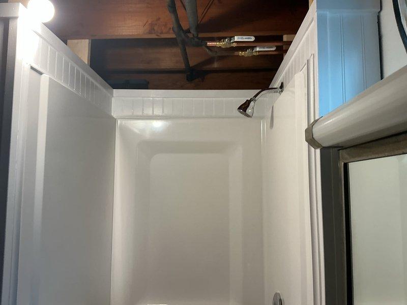 Completed installation of 4-piece shower system in basement bathroom with dimensions of 36" wide, 32" deep, and 76" high. Jackhammered concrete floor to relocate existing shower drain to proper position, installed tub bow, and poured new concrete to restore excavated area. Installed new Moen Chrome Chateau shower valve and faucet assembly with proper water supply connections. Applied wainscoting and casing trim to finish walls surrounding shower enclosure, creating a complete finished appearance. Coordinated work completion ahead of scheduled flooring installation. Temporarily removed existing toilet to facilitate shower installation with plan for reinstallation of new toilet fixture provided on-site.
