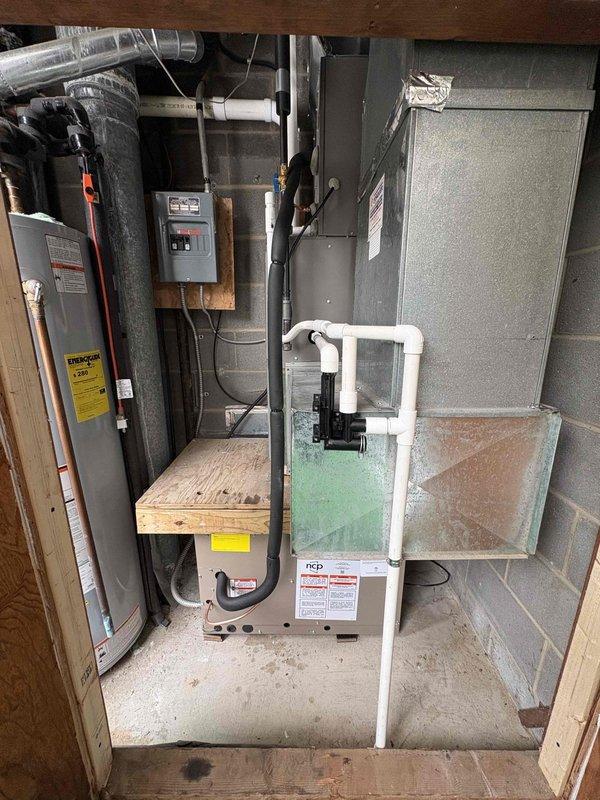 # HVAC Install - Complete System

Completed full installation of residential HVAC system including furnace air handler and through-wall air conditioning unit in basement mechanical room. Installed new air handler unit on elevated wooden platform with proper clearances and mounted gray metal plenum cabinet for air distribution. Configured complete PVC condensate drain system with U-trap configuration and installed condensate pump with black discharge line for proper drainage management. Ran flexible ductwork connections to integrate with existing distribution system. Installed electrical disconnect box and completed all power connections to code requirements. Mounted electrical panel with digital controls on plywood backing for system operation. Routed all refrigerant lines, condensate piping, and electrical conduit in organized manner along concrete block walls. Verified all connections, tested system operation, and confirmed proper drainage flow through condensate management system.
