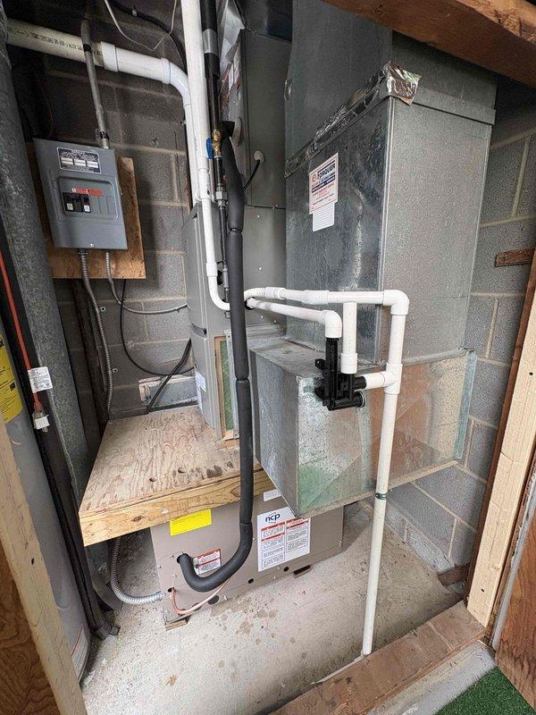 # HVAC Install - Complete System

Completed full installation of residential HVAC system including furnace air handler and through-wall air conditioning unit in basement mechanical room. Installed new air handler unit on elevated wooden platform with proper clearances and mounted gray metal plenum cabinet for air distribution. Configured complete PVC condensate drain system with U-trap configuration and installed condensate pump with black discharge line for proper drainage management. Ran flexible ductwork connections to integrate with existing distribution system. Installed electrical disconnect box and completed all power connections to code requirements. Mounted electrical panel with digital controls on plywood backing for system operation. Routed all refrigerant lines, condensate piping, and electrical conduit in organized manner along concrete block walls. Verified all connections, tested system operation, and confirmed proper drainage flow through condensate management system.