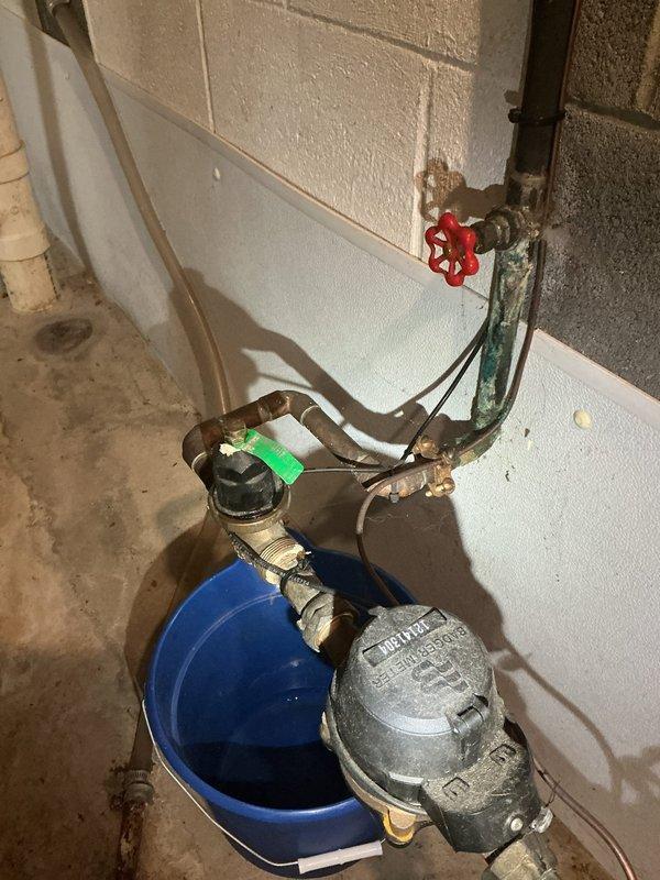 Responded to service call for pressure regulator valve exhibiting slight leakage during water usage. Upon inspection, identified active weeping from the pressure regulator assembly mounted on the main water supply line. Verified system pressure readings using existing gauge, which indicated proper operating range. Assessed condition of brass fittings, valve body, and associated copper piping connections for corrosion and mineral buildup. Documented existing plumbing configuration including red-handled gate valve, water meter, and pressure regulation components. Captured photographic documentation of the pressure regulator setup and gauge readings for service records. Leak was isolated to the pressure regulator valve body during active water flow conditions.