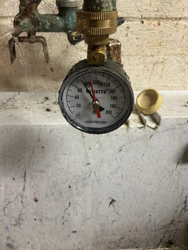 Responded to service call for pressure regulator valve exhibiting slight leakage during water usage. Upon inspection, identified active weeping from the pressure regulator assembly mounted on the main water supply line. Verified system pressure readings using existing gauge, which indicated proper operating range. Assessed condition of brass fittings, valve body, and associated copper piping connections for corrosion and mineral buildup. Documented existing plumbing configuration including red-handled gate valve, water meter, and pressure regulation components. Captured photographic documentation of the pressure regulator setup and gauge readings for service records. Leak was isolated to the pressure regulator valve body during active water flow conditions.
