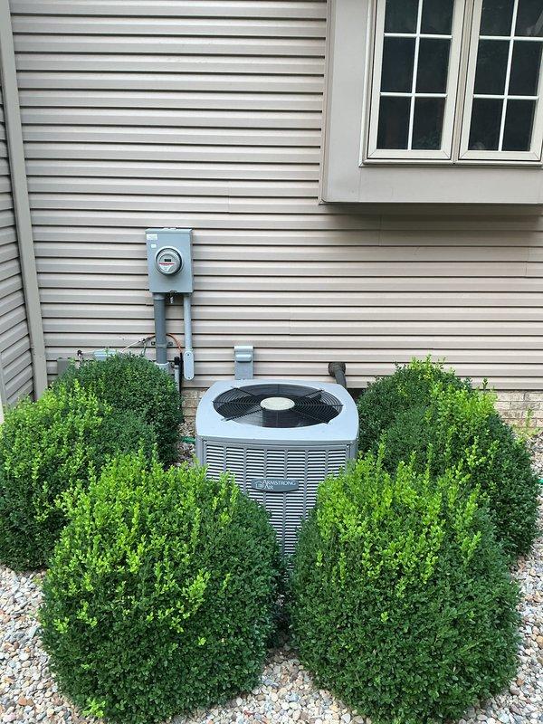 Completed installation of new Carrier HVAC system including furnace, air handler, and outdoor condensing unit. Interior equipment installed in basement with proper venting via white PVC piping, and outdoor AC unit positioned on gravel pad against exterior wall with appropriate electrical disconnect and line set connections. System fully operational with all components properly mounted, leveled, and secured per manufacturer specifications.