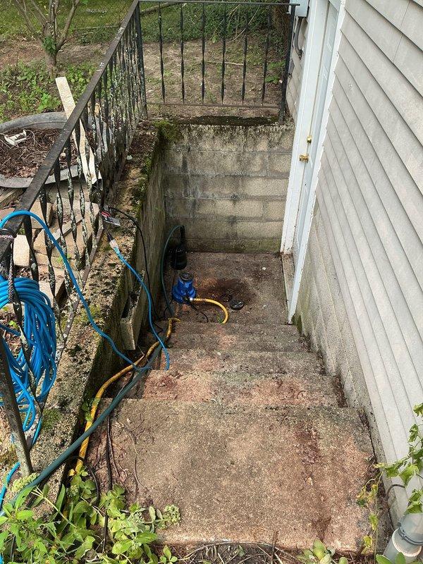 Responded to a non-draining ground water drain located at the bottom of exterior basement stairs near storm door. Upon arrival, found concrete stairwell with significant water staining, moss growth, and organic buildup indicating chronic drainage issues. Customer had been utilizing two pumps during heavy rainfall events to prevent water intrusion into basement due to drain failure.

Inspected drain system at base of stairwell and identified blockage preventing proper storm water discharge. Cleared accumulated debris, sediment, and organic matter from drain opening and line. Verified water flow and drainage capacity restored to functional operation. Tested system to ensure proper water evacuation from stairwell area, eliminating need for temporary pump usage during precipitation events.