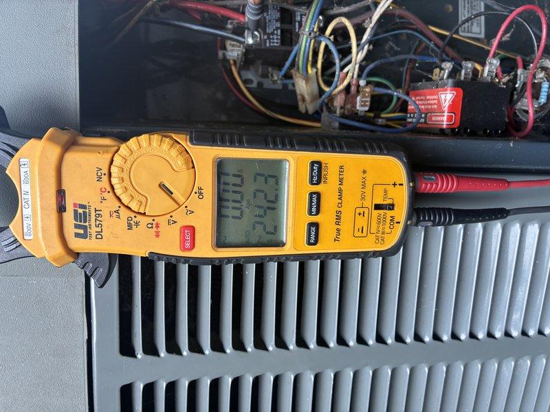 Completed scheduled preventative maintenance cooling visit on 2-year-old outdoor air conditioning unit. Performed comprehensive system inspection including electrical diagnostics using clamp meter to verify amperage draws and voltage readings across key components. Measured compressor amperage at 0.33A and monitored system performance parameters. Inspected capacitor condition, noting visible corrosion and rust on terminal connections with degraded wiring insulation present. Evaluated condenser coil fins and heat exchanger surfaces. Observed accumulated debris, dirt, and organic matter throughout unit housing with evidence of extended outdoor exposure causing weathering to internal components. Documented multicolored electrical wiring configuration and connection integrity across control board terminals. Unit operational at time of service completion with all findings photographed for maintenance records.