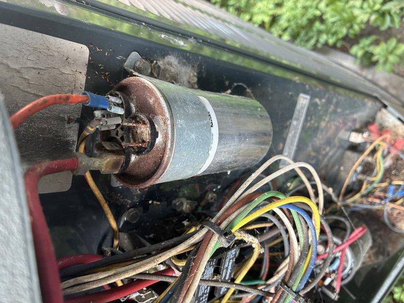 Completed scheduled preventative maintenance cooling visit on 2-year-old outdoor air conditioning unit. Performed comprehensive system inspection including electrical diagnostics using clamp meter to verify amperage draws and voltage readings across key components. Measured compressor amperage at 0.33A and monitored system performance parameters. Inspected capacitor condition, noting visible corrosion and rust on terminal connections with degraded wiring insulation present. Evaluated condenser coil fins and heat exchanger surfaces. Observed accumulated debris, dirt, and organic matter throughout unit housing with evidence of extended outdoor exposure causing weathering to internal components. Documented multicolored electrical wiring configuration and connection integrity across control board terminals. Unit operational at time of service completion with all findings photographed for maintenance records.