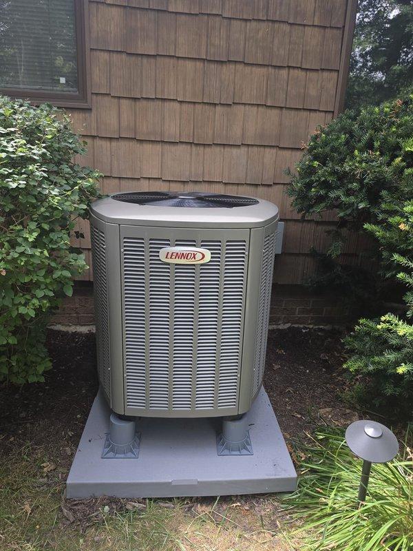 Completed installation of Lennox heat pump system integrated with existing oil furnace setup. Indoor air handler unit mounted in basement utility area with refrigerant lines, electrical connections, and ductwork professionally installed and secured. Outdoor condenser unit positioned on concrete pad against exterior wall with proper clearances maintained for airflow and serviceability.