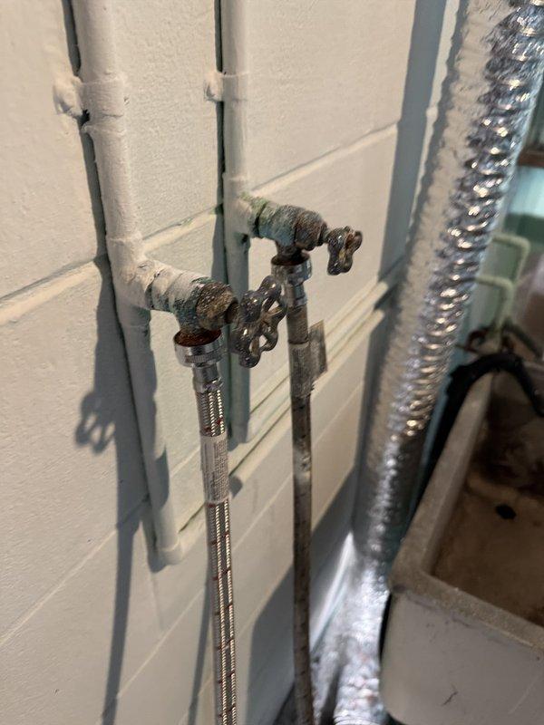 Responded to a leaking water valve in the basement that supplies the washing machine connection. Upon inspection, found corroded shut-off valves with visible deterioration and staining. Replaced the old, weathered valves with new brass quarter-turn shut-off valves featuring red handles and connected them with flexible braided stainless steel supply lines. Tested the new installation for proper operation and verified no leaks were present at the connections or valve bodies.