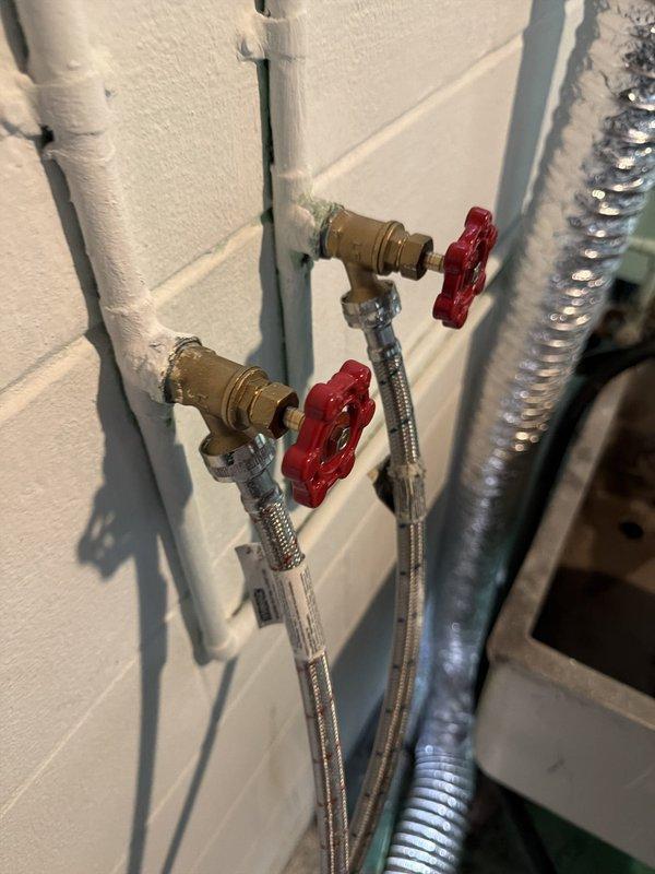 Responded to a leaking water valve in the basement that supplies the washing machine connection. Upon inspection, found corroded shut-off valves with visible deterioration and staining. Replaced the old, weathered valves with new brass quarter-turn shut-off valves featuring red handles and connected them with flexible braided stainless steel supply lines. Tested the new installation for proper operation and verified no leaks were present at the connections or valve bodies.