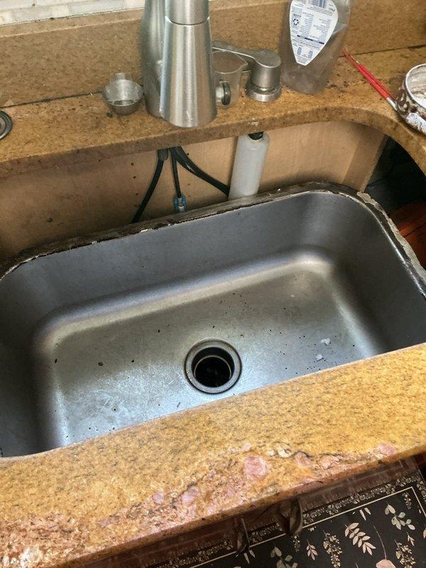 Responded to service call for undermount sink failure that caused damage to associated plumbing and garbage disposal system. Upon inspection, found that the sink had detached from the countertop, compromising the drain assembly connections and potentially affecting the disposal unit. Assessed the aging plumbing infrastructure (11-33 years old) and documented existing conditions through photography, including structural gaps near ceiling junction and current state of sink basin with visible debris. Provided customer with evaluation findings and discussed necessary repairs to restore proper function and secure mounting of undermount sink assembly.