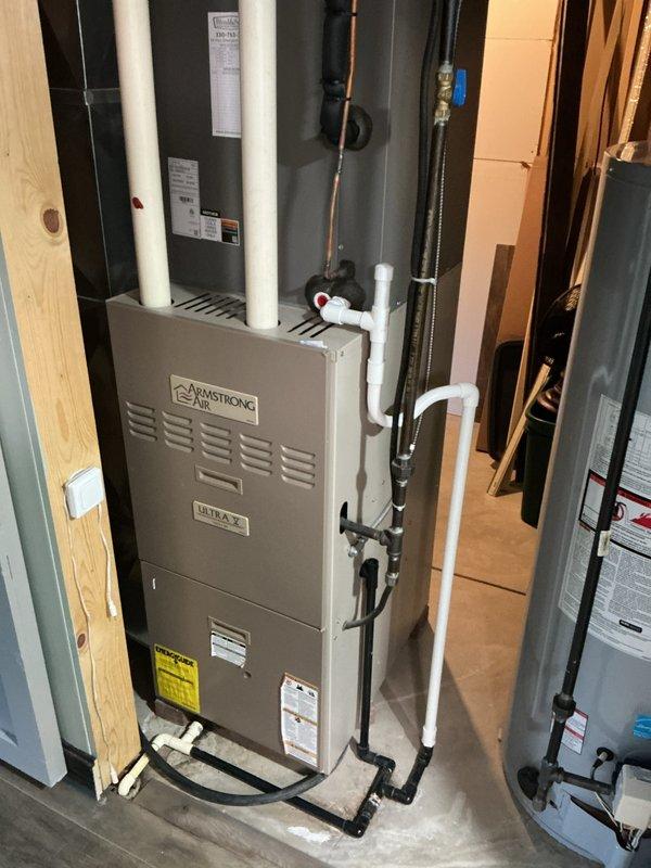 Completed installation of new Armstrong Ultra SX 90% AFUE furnace in residential utility room. Unit positioned and secured in basement mechanical space alongside existing water heating equipment, with proper clearances maintained per manufacturer specifications. Connected white PVC venting pipes vertically through structure for combustion air intake and exhaust, installed condensate drainage lines, and completed all electrical connections. Verified proper operation of all safety controls, confirmed adequate airflow, and ensured unit is functioning within specified parameters.