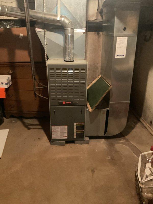 Responded to no cooling complaint on 18-year-old residential air conditioning system. Upon arrival, found outdoor condenser unit with fan motor operating but system failing to produce cooling. Observed vegetation growth obstructing airflow around condenser coils and internal components. Removed access panel to inspect electrical system, including capacitor and wiring connections. Documented condition of unit with photographs showing aged equipment, compromised internal components, and environmental debris accumulation affecting system performance.