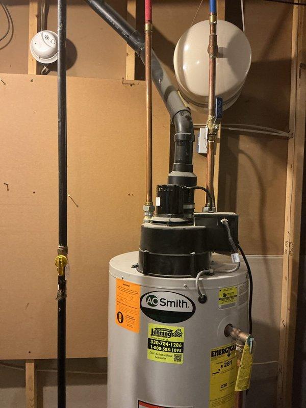 Responded to service call for leaking A.O. Smith tanked water heater with unusual dual-fuel configuration having both gas and electric connections. Conducted thorough assessment of the unit and photographed existing installation showing water heater positioned in unfinished basement with associated plumbing connections, black pump assembly, copper supply lines with color-coded sections, white expansion tank, and pressure relief piping. Documented complete system setup including all pipe routing, fittings, and component placement to provide comprehensive replacement estimate for failed unit.
