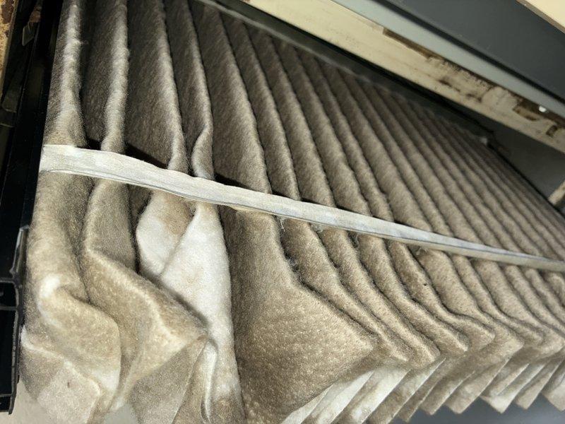 Completed routine MVP cooling maintenance visit for residential air conditioning system. Inspected and documented air filter condition, showing moderate dust accumulation with visible particulate buildup in chevron pattern indicating normal filtration operation. Verified electrical disconnect box and external components, confirming proper installation and accessibility of safety disconnect switch with dual conduit connections to outdoor unit.