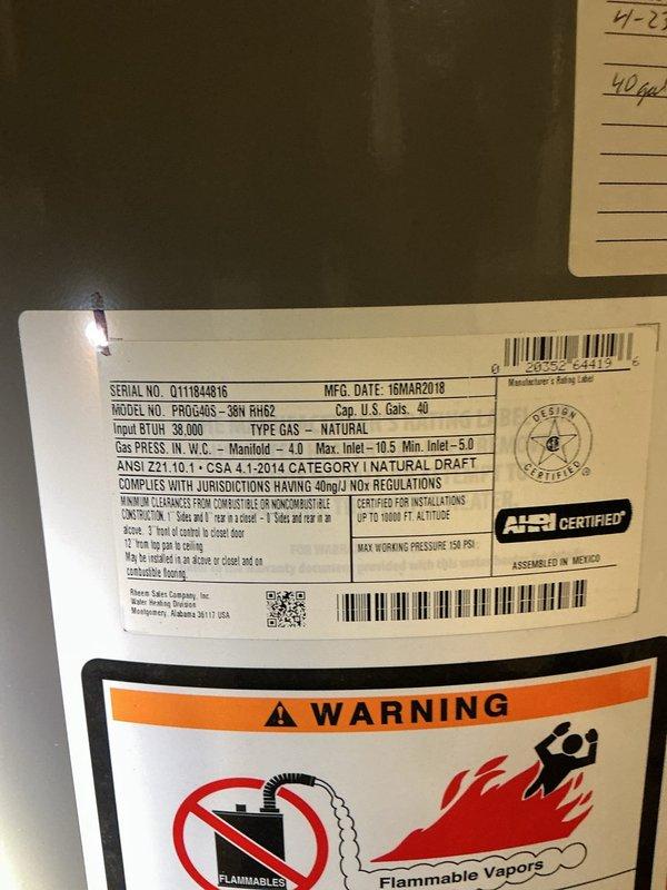 Responded to service call for leaking 40-gallon natural gas water heater (Model PROG40S-36N RH62) manufactured in March 2018. Upon inspection, identified active leak affecting entire home's hot water supply in basement utility area. Documented equipment specifications, safety labels, and installation configuration including pressure relief valve, gas connections, and copper supply lines with blue pressure regulator. Photographed unit condition, surrounding concrete floor showing water damage and staining, and proximity to HVAC system in mechanical room with concrete block walls.