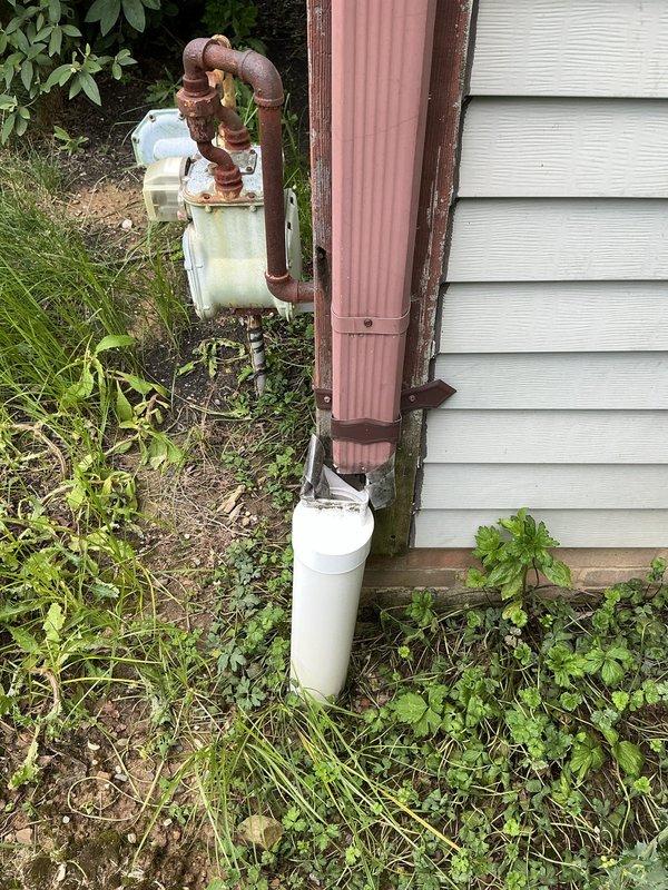 Conducted site inspection and assessment of exterior drainage system. Customer requested estimate for downspout repair and installation of rain barrel diverter kit. Documented existing conditions including deteriorated metal plumbing assembly with extensive rust corrosion on exterior wall-mounted components, compromised downspout system with corrugated pink discharge pipe, and white catch basin at grade level. Photographed rusted valve assembly and connecting pipes requiring replacement, as well as surrounding vegetation encroachment affecting drainage infrastructure. Provided professional recommendations for downspout system rehabilitation and rain barrel diverter installation to improve water management and extend system longevity.