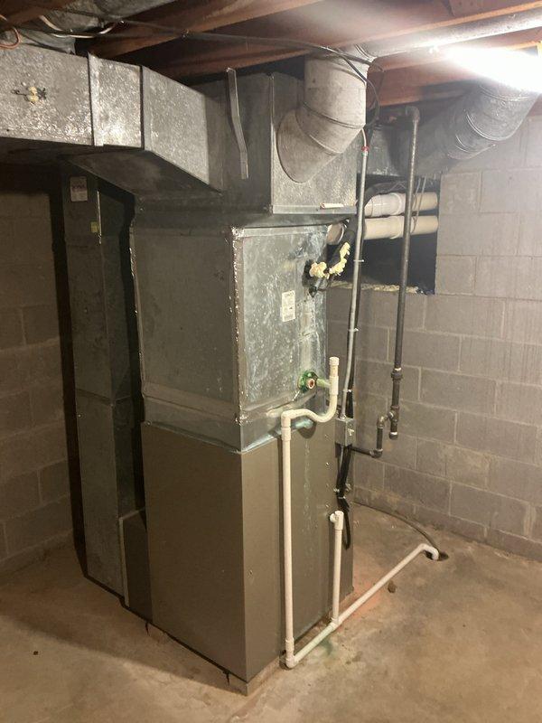 Completed installation of two outdoor Lennox air conditioning condenser units positioned side by side on concrete pads against exterior brick wall, with proper clearance spacing between units and building structure. Indoor coil installation performed in basement mechanical room, integrated with existing furnace system, including proper refrigerant line connections, condensate drain piping with white PVC, and electrical connections to support dual-zone cooling system operation.