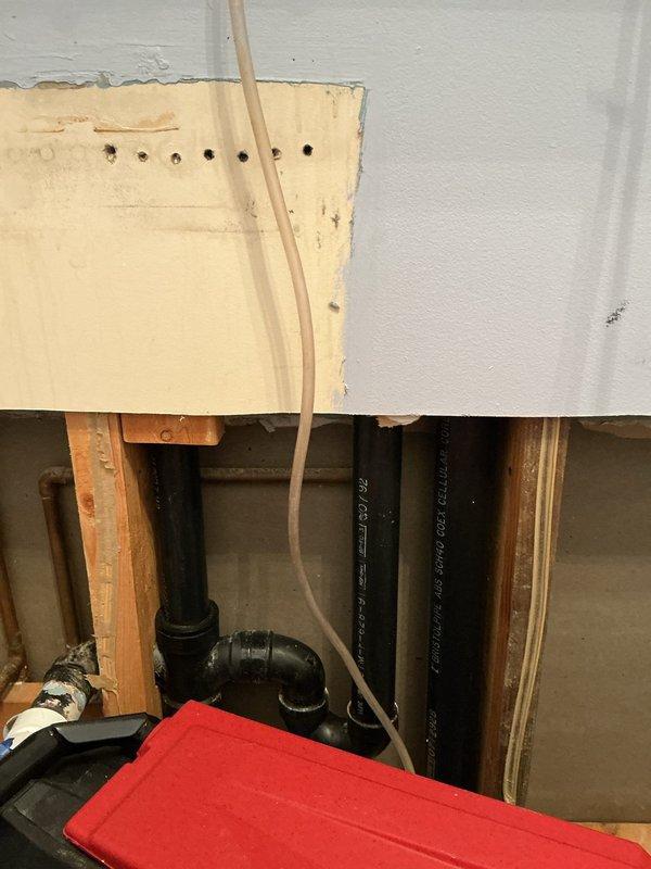 Responded to water leak emergency originating from black PVC pipe with visible pooling on floor. Accessed plumbing system through wall opening to locate leak source at pipe connection. Installed new shut-off valve assembly at water supply line beneath kitchen cabinets, including chrome quarter-turn valves with oval handles mounted in recessed outlet box. Connected flexible supply line to new valve installation. Tested system for proper operation and verified no active leaks at connection points. Restored wall access panel and secured all plumbing connections.