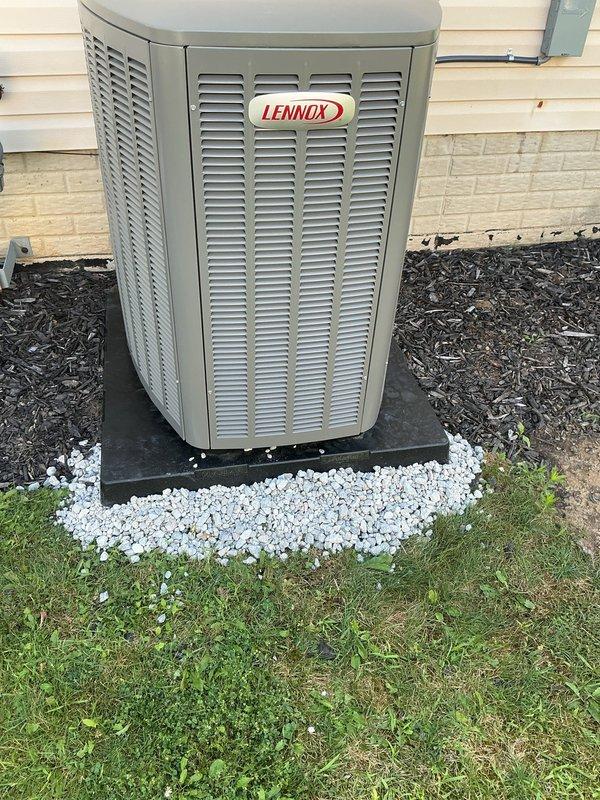 Responded to callback on 28-day-old Lennox installation experiencing loud banging noise upon startup. Diagnosed unit settling and pad instability as root cause of mechanical noise. Leveled and stabilized condenser unit using handjack tool, added gravel base material beneath existing concrete blocks and black composite pad to eliminate movement and ensure proper drainage. Verified unit operation with no abnormal sounds, confirmed level installation and secure mounting. System operating within normal parameters.