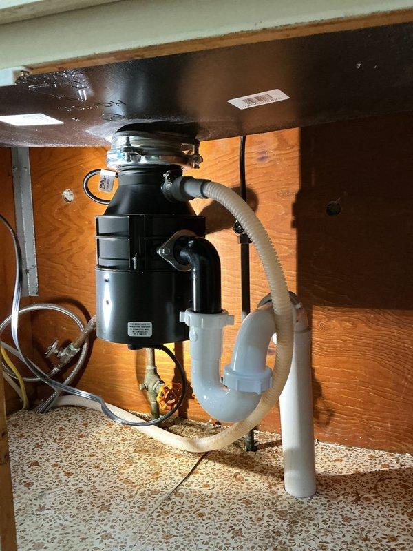 Completed full kitchen sink replacement and plumbing system upgrade. Removed existing sink and installed new Allen + Roth 33"x22" single bowl drop-in sink with black finish. Mounted and connected customer-supplied matte black faucet with coiled hose attachment, including installation of new shut-off valves and supply lines. Installed new black garbage disposal with matching disposal mount and electrical connection. Replaced all under-sink plumbing with new trap assembly and PVC drainage components. Drilled new drain line penetration through cabinet base as needed. In basement, removed existing rubber sand tee from 1-1/2" copper drain line and re-plumbed connection to vent stack using new PVC piping to ensure proper drainage and code compliance. All components tested and verified operational upon completion.