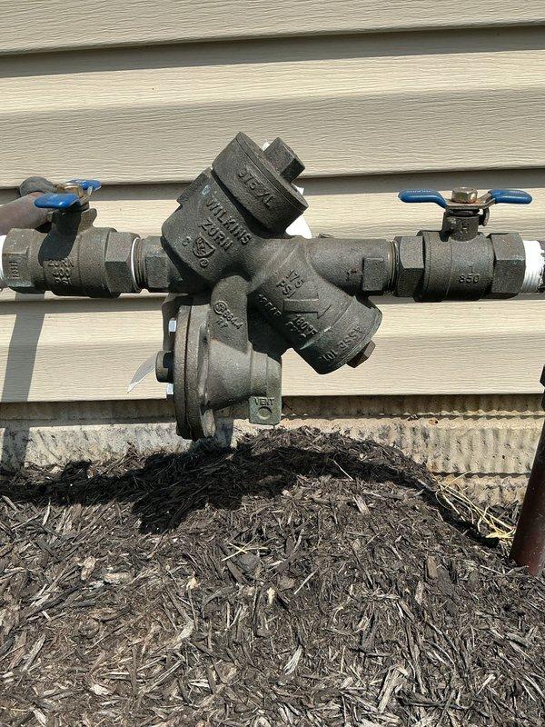 Responded to service call for backflow prevention system malfunction. Upon inspection, evaluated the Wilkins Zurn backflow preventer assembly rated at 375 PSI, including ball valves, Y-strainer configuration, and associated piping mounted at exterior foundation level. Documented current system condition with photographs and provided estimate for necessary repairs to restore proper backflow prevention functionality.
