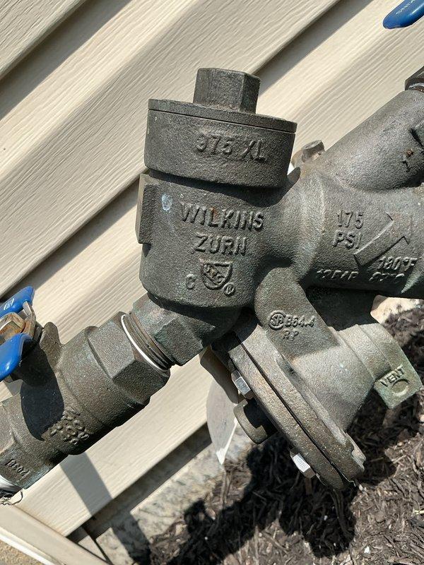 Responded to service call for backflow prevention system malfunction. Upon inspection, evaluated the Wilkins Zurn backflow preventer assembly rated at 375 PSI, including ball valves, Y-strainer configuration, and associated piping mounted at exterior foundation level. Documented current system condition with photographs and provided estimate for necessary repairs to restore proper backflow prevention functionality.